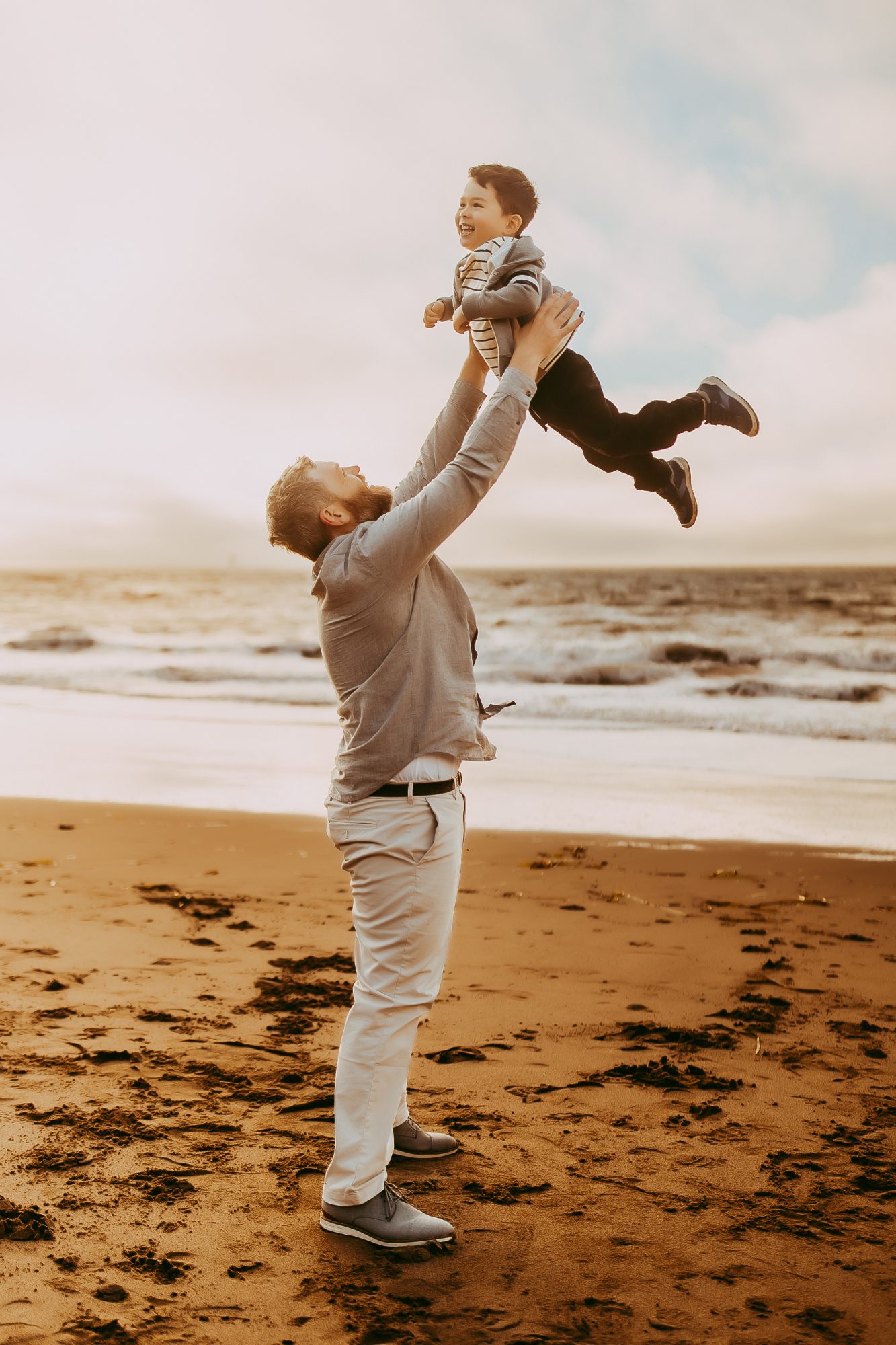 Shefali Parekh | Capturing Joy and Laughter: The Family Session at Baker Beach A father lifting his son on a sandy beach