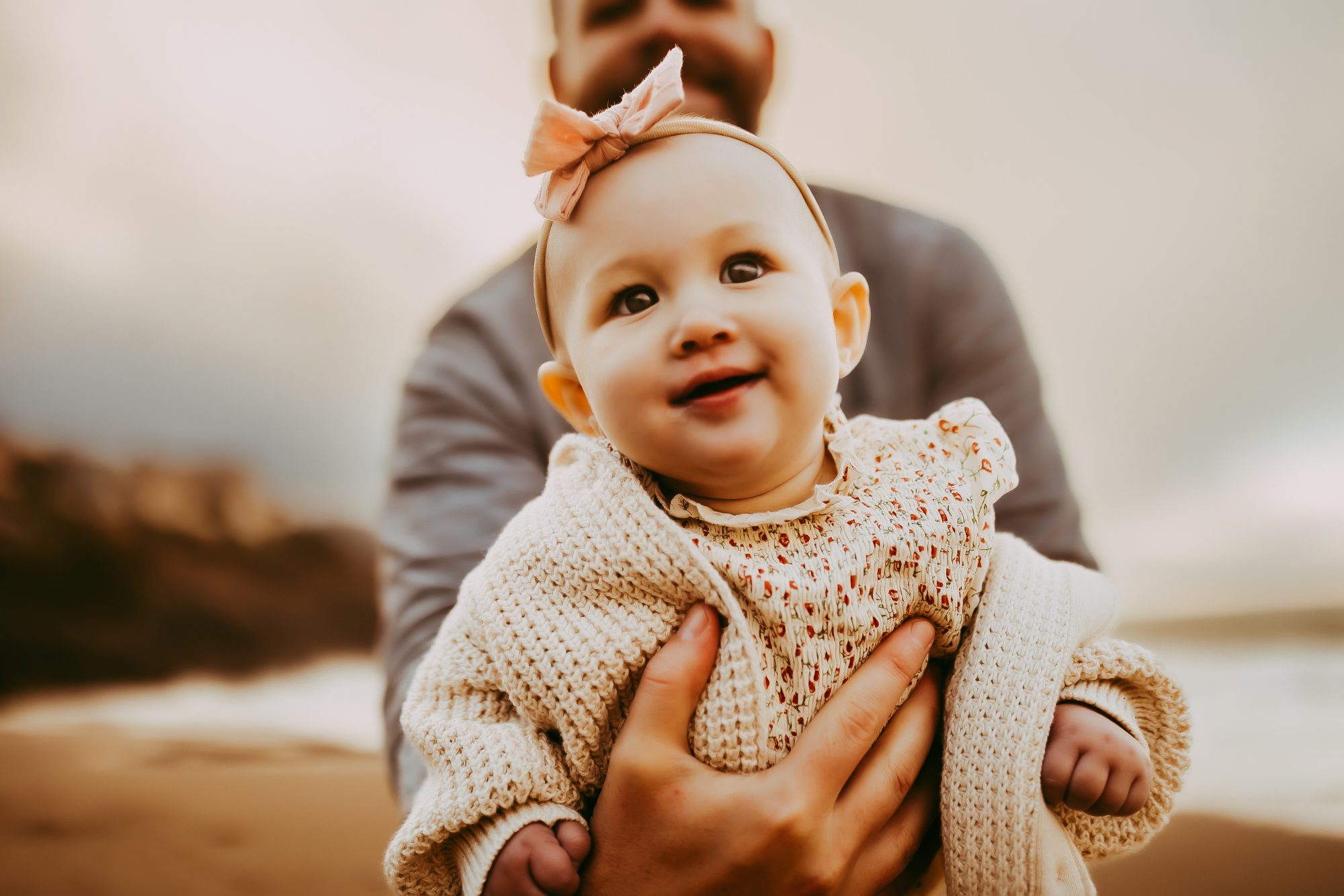 Shefali Parekh | Capturing Joy and Laughter: The Family Session at Baker Beach A man cradling a baby on a sandy beach