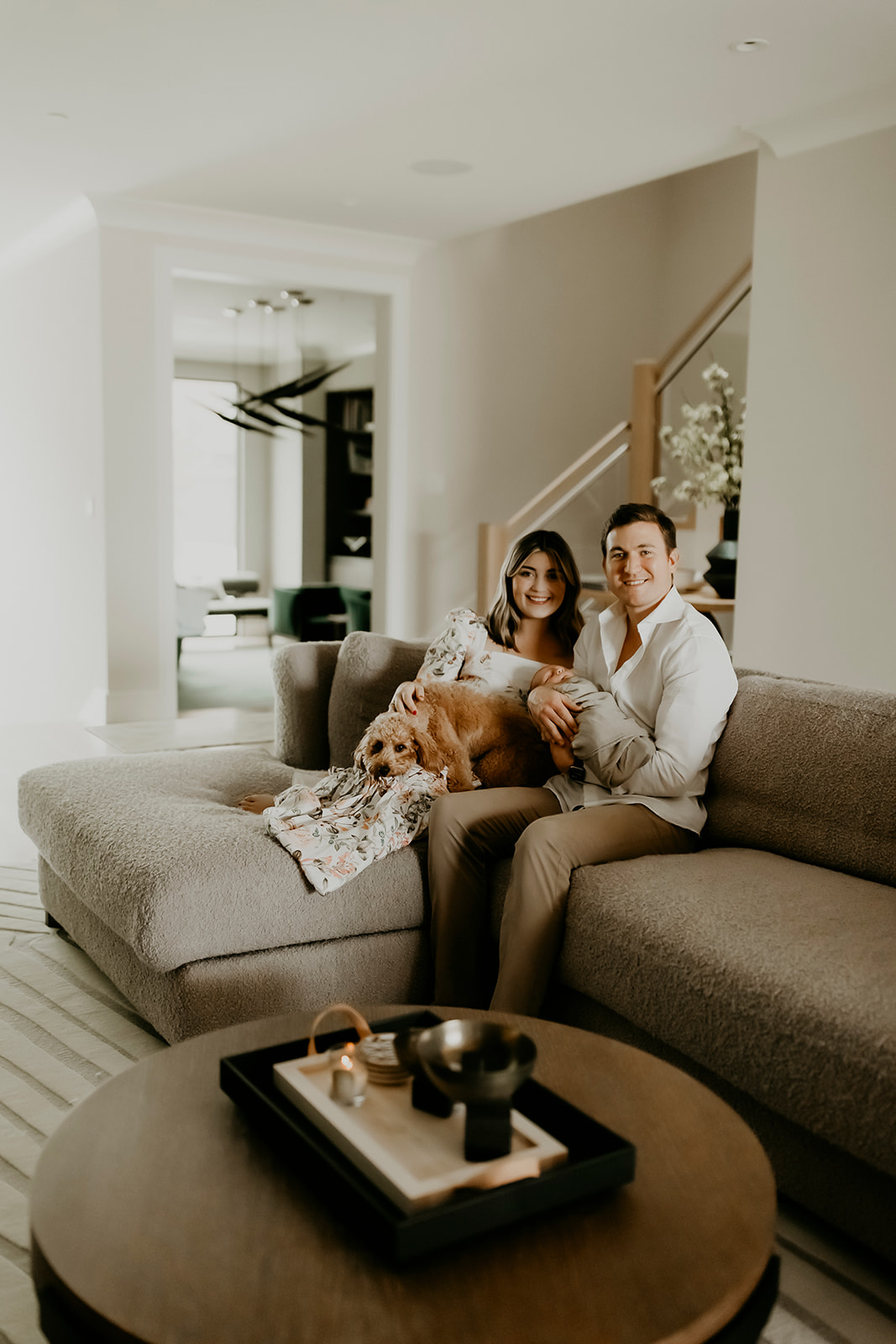 Shefali Parekh | Heartwarming In-Home Newborn Session: Maggie & Alex Black in Cow Hollow, San Francisco Couple sitting on couch holding their dog & newborn
