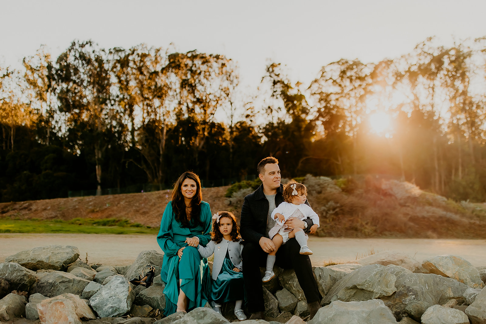 Shefali Parekh | The Best Location for Family Photography: Crissy Field Family sitting on rock with sunset in background for family photos in San Francisco