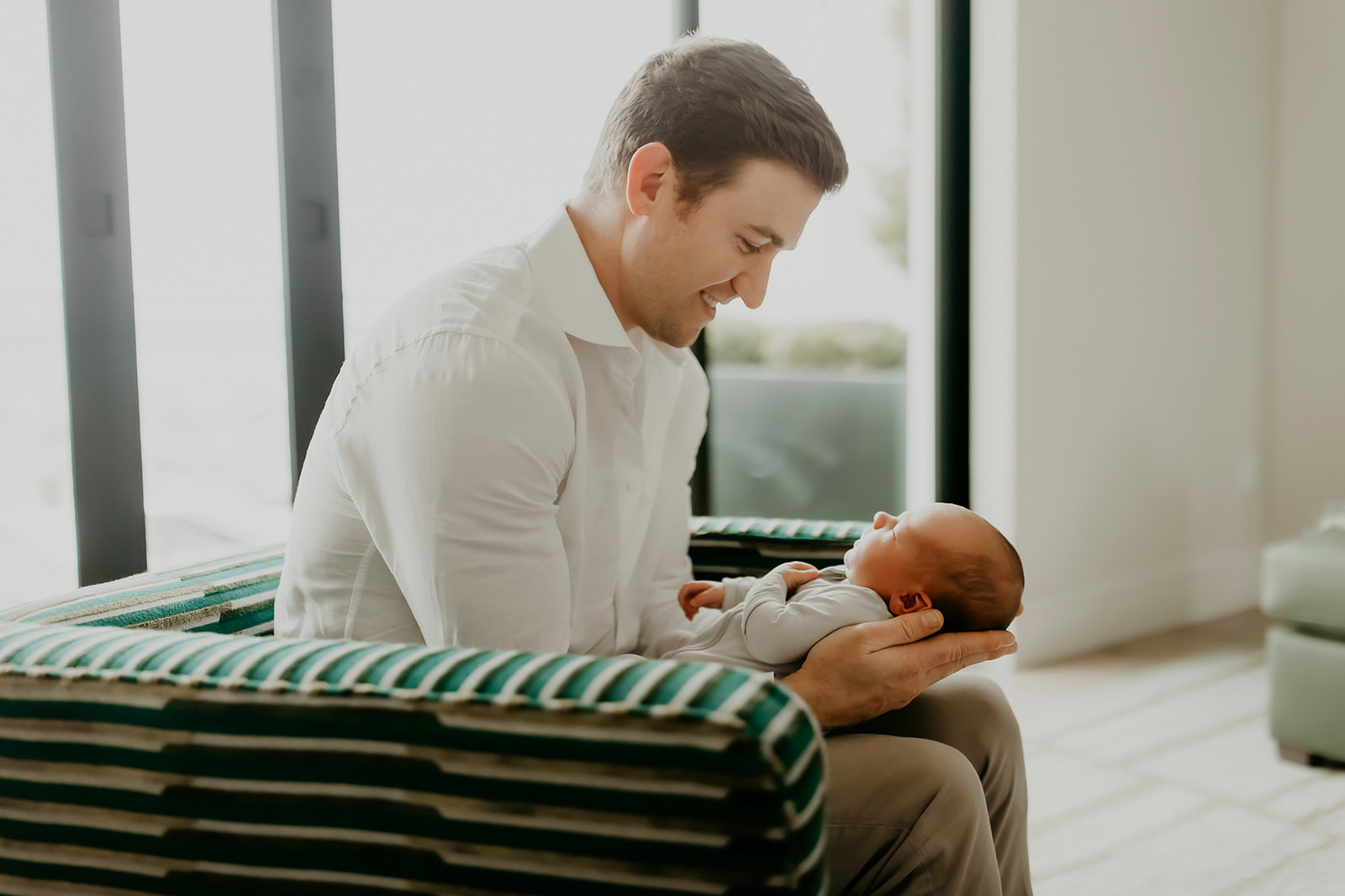 Shefali Parekh | Heartwarming In-Home Newborn Session: Maggie & Alex Black in Cow Hollow, San Francisco Man sitting on sofa looking at his newborn child